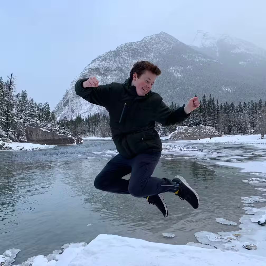 A picture of me in winter jumping and smiling in front of a mountain