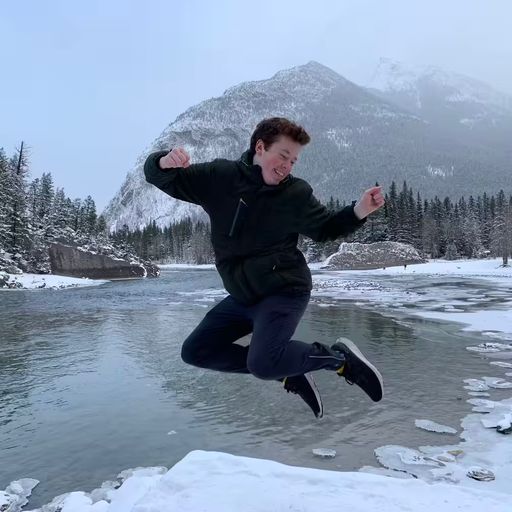 A picture of me in winter jumping and smiling in front of a mountain